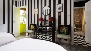 A room with a checkered floor, a bed, two chairs, a console table with lamps, a mirror, and a door leading to another room. - Fell End - Sleeping 8+5 guests in 4 bedrooms (Brampton)