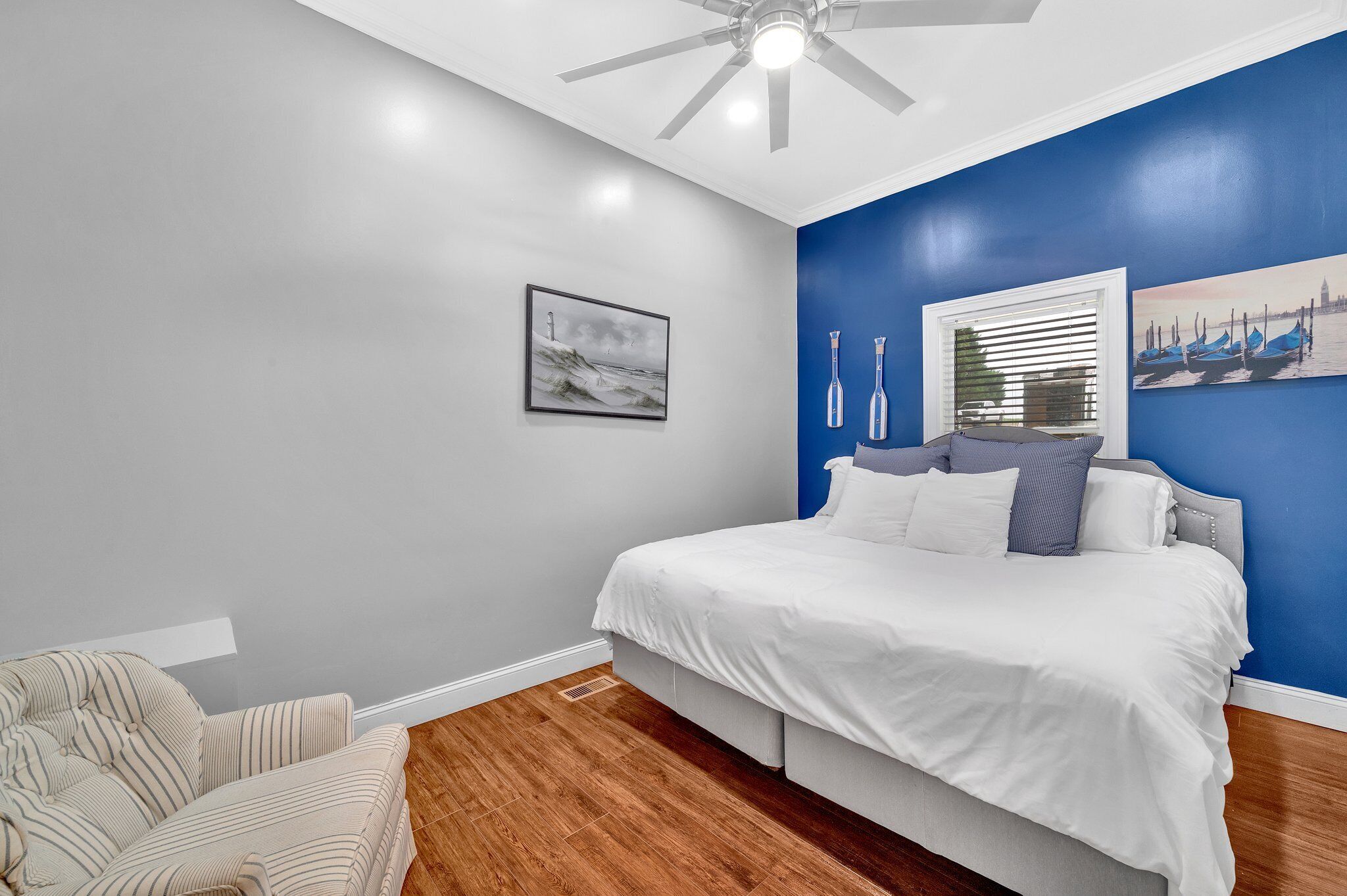 Quarto com cama, cadeira, ventilador de teto e obras de arte nas paredes.
