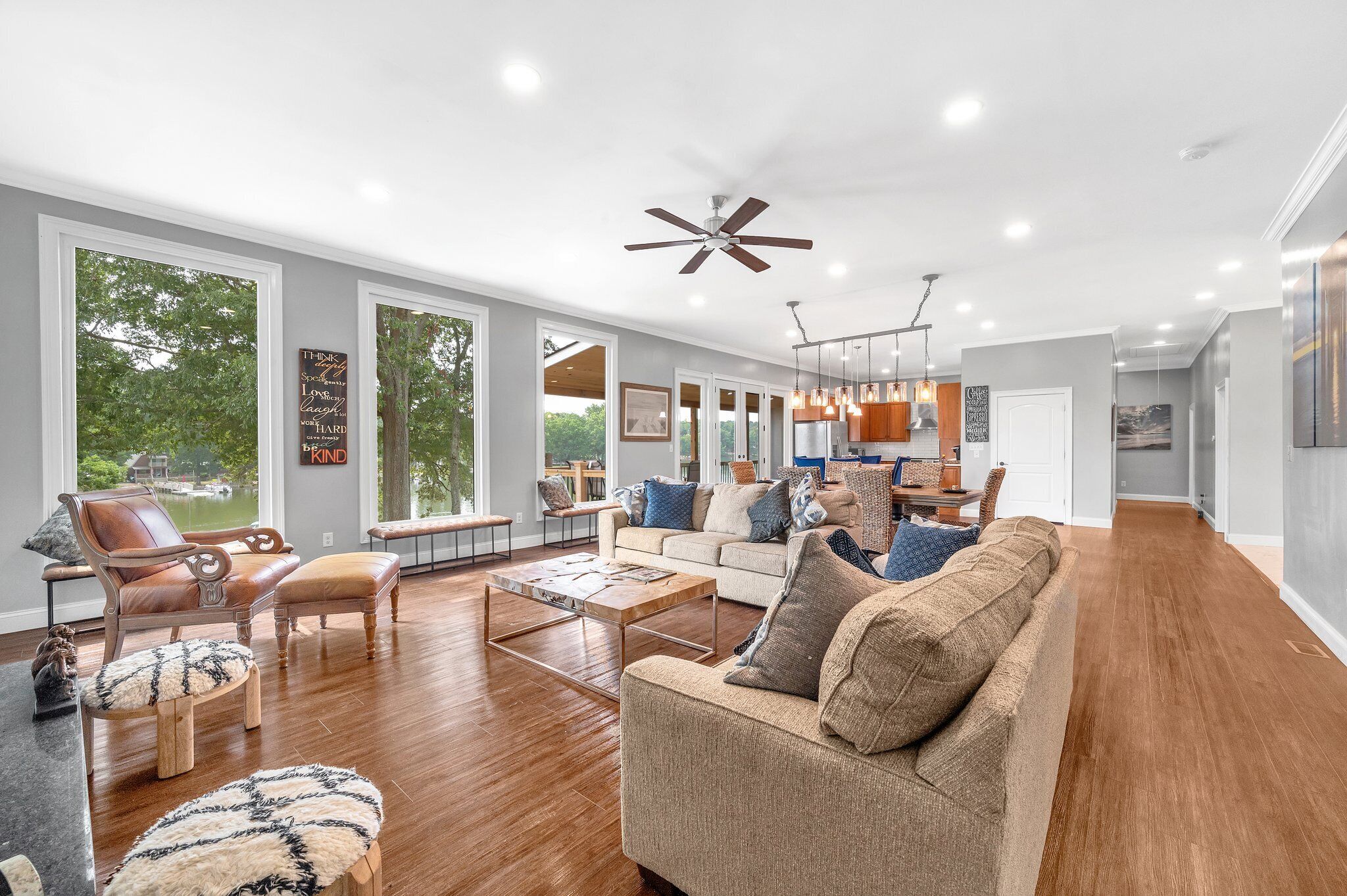 A spacious living room with a large window, a ceiling fan, and a wooden floor.