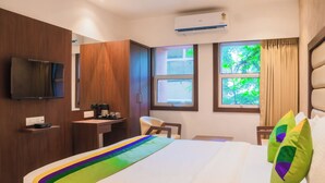 Habitación de hotel con cama, escritorio, silla, televisor y ventana con cortinas.
