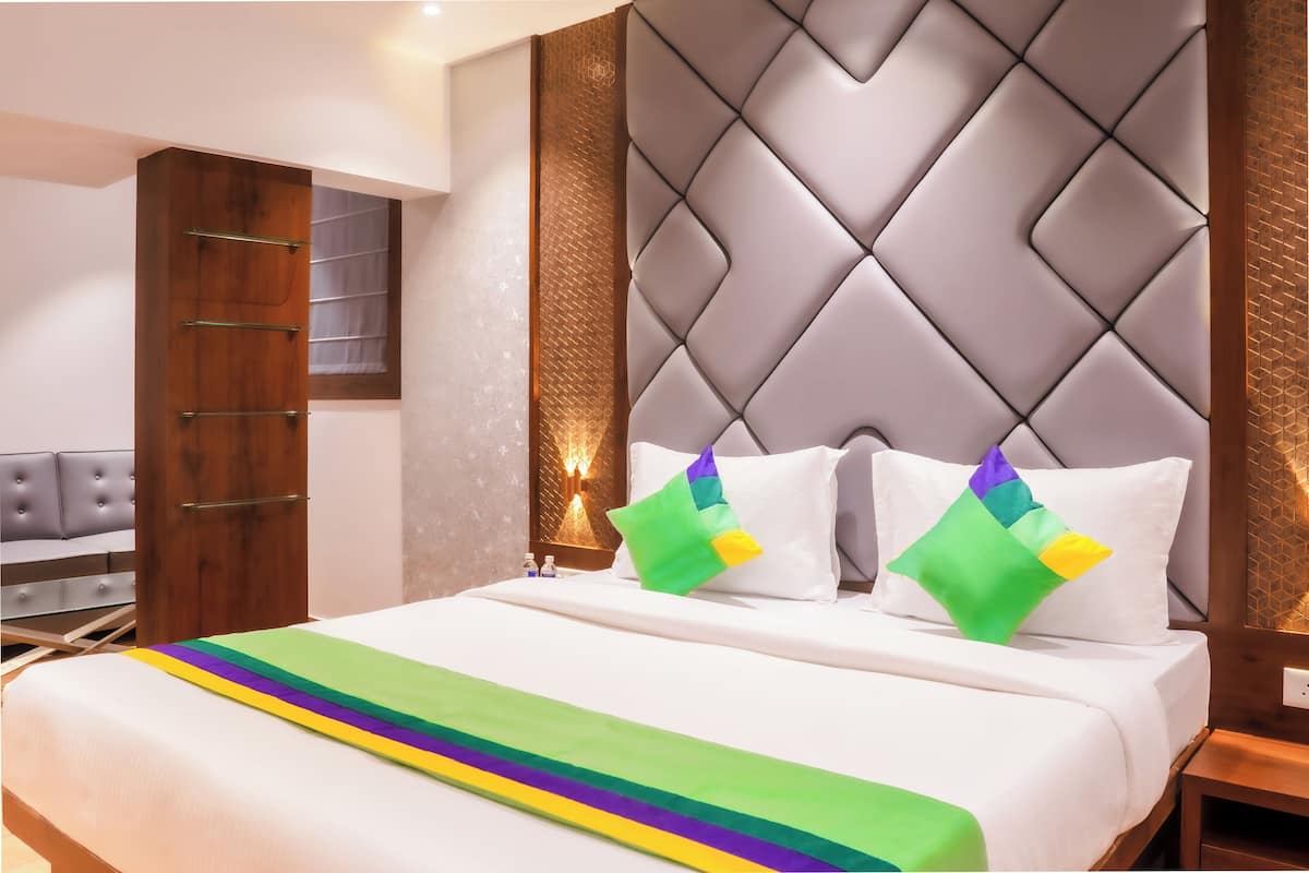 A hotel room with a bed, a wooden wardrobe, a grey upholstered sofa, and a wall with a textured pattern.
