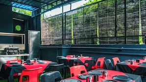 Un área de comedor al aire libre con mesas dispuestas para varios comensales, con manteles y sillas rojas y negras.