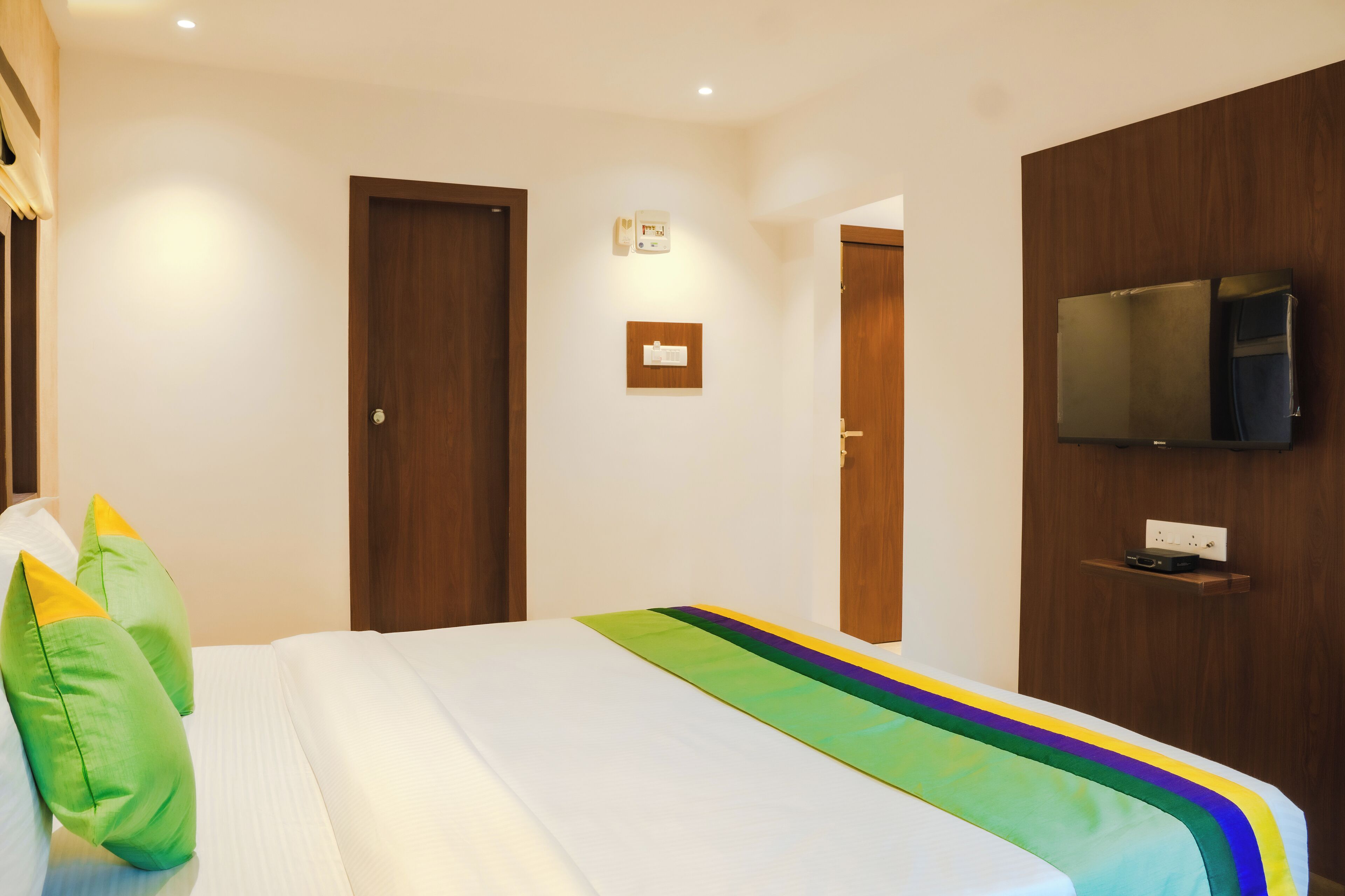Una habitación de hotel con una cama, un televisor montado en la pared y una puerta.