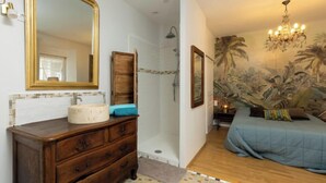 Un dormitorio con un espejo grande, cómoda de madera, cama con ropa de cama azul y un mural de palmeras.