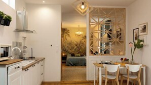 Cocina compacta con armarios blancos, microondas y cafetera. Hay un comedor con mesa y sillas de madera, y un separador decorativo de madera.