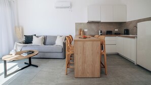 A modern kitchen with white cabinets, a wooden dining table, and a grey sofa in the living area. - Boutique villa with private pool in Alonissos island, Greece. Stunning sea view. (Votsi)