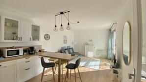Ett modernt kök med vita skåp, ett matbord i trä och barstolar. Här finns en mikrovågsugn, en kaffebryggare och ett kylskåp.