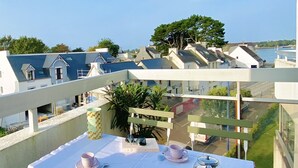 En balkong med ett bord dukat för te, med utsikt över ett bostadsområde med hus och en klar himmel.