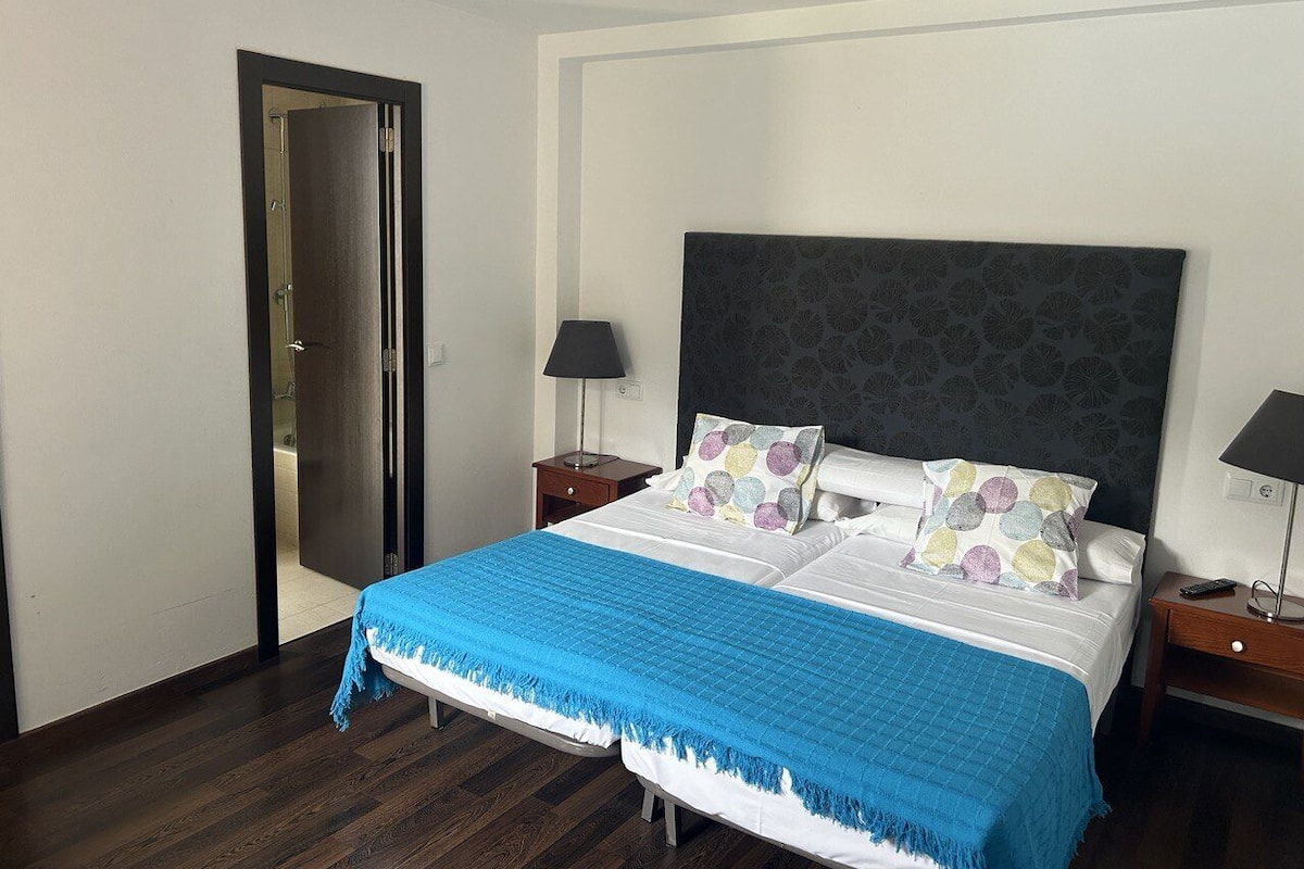 Ein Hotelzimmer mit einem großen Bett, zwei Nachttischen, einer Zimmertür und einem gemusterten Kopfteil.