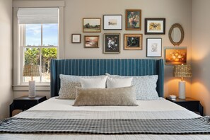 A neatly arranged bedroom with a large bed, a window with a view, and a wall adorned with framed pictures. - New* Seabrook's Grove Cottage: Dog Friendly, Hot Tub! (Pacific Beach)