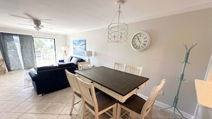 Un'area pranzo con un tavolo in legno scuro e sedie in legno chiaro, una ventola a soffitto, una sveglia a muro e un appendiabiti.