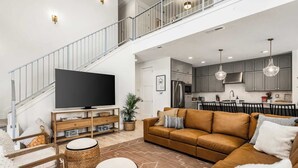 Un espacio habitable amplio con un televisor de pantalla plana grande, un sofá de cuero marrón y una escalera que conduce a un piso superior.