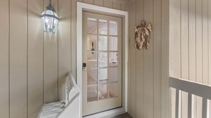A wooden door with a glass panel, a white bench, and a wall-mounted light fixture. - Seabrook Exclusives | 1144 Summerwind (Johns Island)