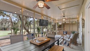 A covered patio area with a dining table, chairs, a TV, and a ceiling fan. - Seabrook Exclusives | 1144 Summerwind (Johns Island)