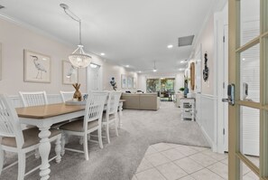 A dining area with a wooden table and white chairs, a chandelier, and framed artwork on the walls.