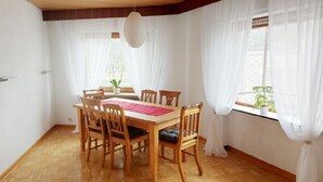 A dining area with a wooden table and chairs, white curtains, and a hanging light fixture. - fewo-herrheinspaziert (Oberwesel)