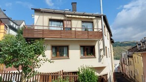 A two-story building with a balcony on the upper floor, surrounded by a wooden fence and greenery. - fewo-herrheinspaziert (Oberwesel)