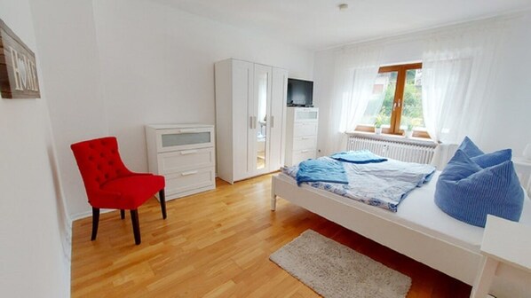 A bedroom with a bed, a red chair, a white wardrobe, and a television. - fewo-herrheinspaziert (Oberwesel)