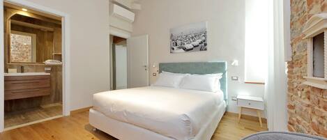 A bedroom with a large bed, a wooden floor, a white dresser, and a brick wall.
