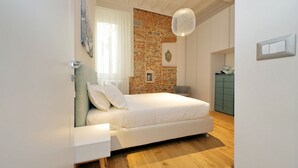 A bedroom with a bed, a nightstand, a dresser, a brick wall, a wooden ceiling, and a hanging light fixture. - Santa Croce Gem w/ Chic Decor & Historic Charm (Florence)
