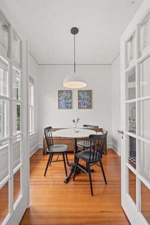 A dining area with a round table, four chairs, a hanging light fixture, and two framed artworks on the wall. - The Adaline #8 - Luxury Second Floor Bayshore Apt! (Tampa)