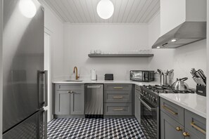 Una cocina moderna con gabinetes grises, electrodomésticos de acero inoxidable, piso a cuadros blanco y negro y una lámpara colgante.