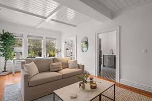 Un salón amplio con un sofá beige, una mesa de centro con objetos decorativos y ventanas grandes que ofrecen vistas a la vegetación.