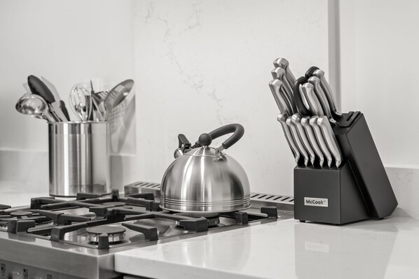 A kitchen with a gas stove, a kettle, a utensil holder, and a knife block.