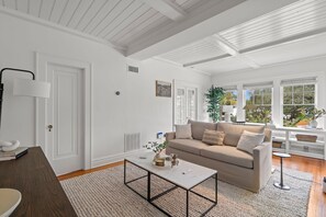Ein geräumiges Wohnzimmer mit einem beige farbenen Sofa, einem Couchtisch und einem großen Fenster mit Blick ins Freie.