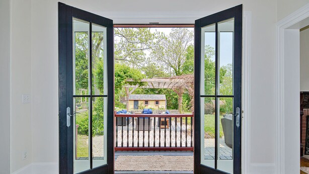 Une pièce dotée d’une grande porte vitrée donnant sur un patio extérieur avec une terrasse en bois et une pergola.