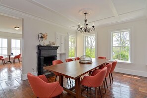 A dining room with a large wooden table, six red chairs, a black fireplace, and large windows with a view of trees.