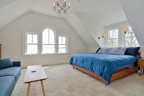 A bedroom with a large bed, a small table, a sofa, and a chandelier.