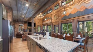 A spacious kitchen with granite countertops, wooden cabinets, and a large island. There is a dining area with wooden tables and chairs, and a fireplace. - Smoky Mtn Haven w/Indoor Pool, Theater, Game Room (Sevierville)
