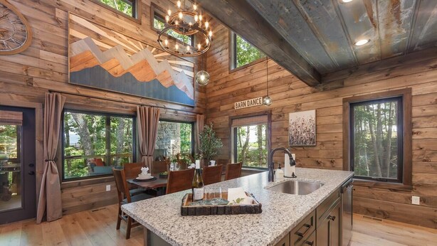 A rustic cabin interior with a kitchen, dining area, and a large window overlooking a forest. - Smoky Mtn Haven w/Indoor Pool, Theater, Game Room (Sevierville)