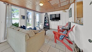 Een gezellige woonkamer met een bank, rode fauteuils, een televisie en een groot raam met uitzicht op de omgeving.