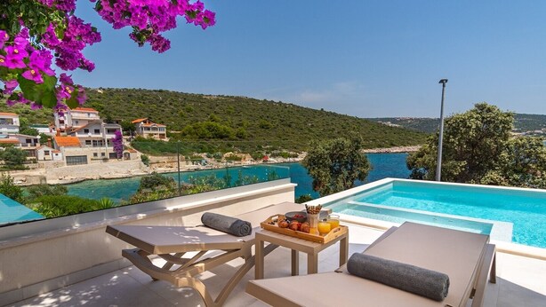 A poolside area with lounge chairs, a table with breakfast items, and a view of a coastal landscape. - Stylish and luxurious beachfront villa Larisa with private pool and Whirlpool (Rogoznica)