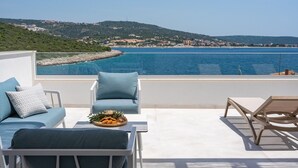 A terrace with a view of the sea, featuring two blue cushioned chairs, a wooden table with a plate of food, and a sun lounger. - Stylish and luxurious beachfront villa Larisa with private pool and Whirlpool (Rogoznica)