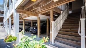 Uma área de estacionamento coberta, com vigas de madeira e uma escadaria que leva a um andar superior.