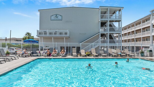 Uma área de piscina com espreguiçadeiras e um edifício com a inscrição 'CW Condominiums'.
