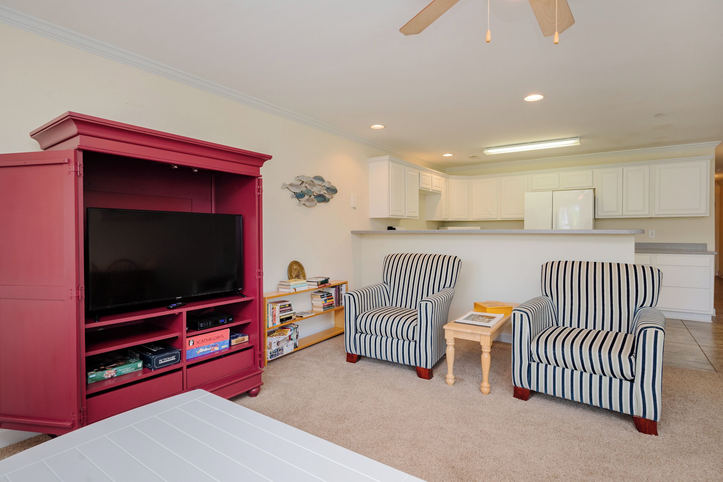 A living room with a red entertainment unit, two striped armchairs, a small table, and a flat-screen TV.