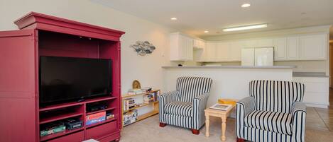A living room with a red entertainment unit, two striped armchairs, a small table, and a flat-screen TV.