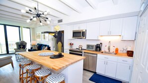 A modern kitchen with white cabinets, a wooden island with bar stools, stainless steel appliances, and a ceiling fan. - Jada 2b 1 Bedroom Condo by RedAwning (Ocean City)