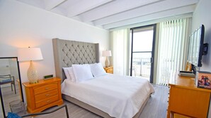 A hotel room with a large bed, two bedside tables, a mirror, a TV, and a balcony with curtains. - Jada 2b 1 Bedroom Condo by RedAwning (Ocean City)