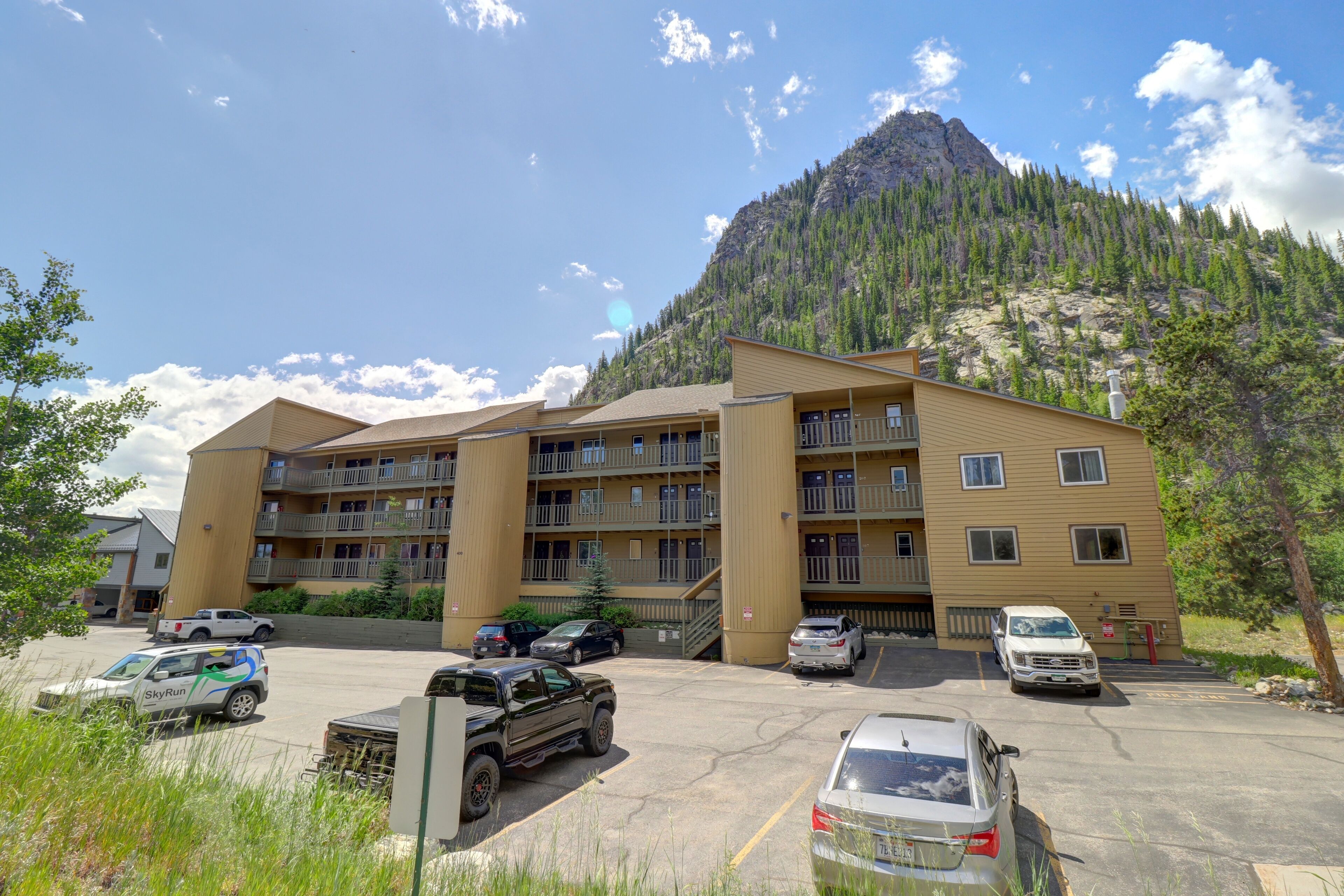 A multi-story hotel with a parking lot, surrounded by mountains and greenery.
