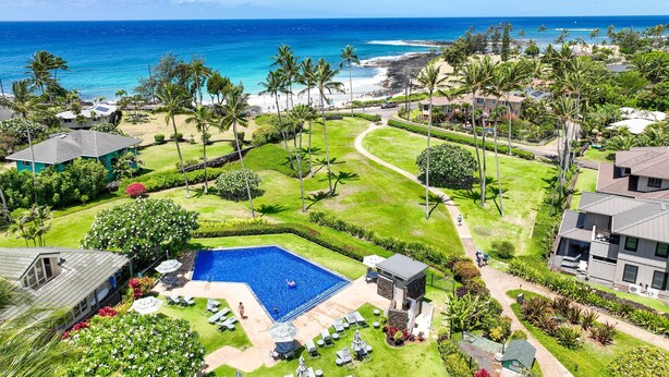 A resort with a large swimming pool, lush greenery, and a view of the ocean.