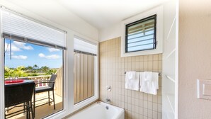 A bathroom with a bathtub, a window, and a view of a balcony with a table and chairs.