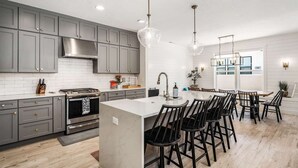 A modern kitchen with grey cabinets, a central island with bar stools, and pendant lighting. - Desert Brooke Villa 6 Bedroom Townhouse (St. George)