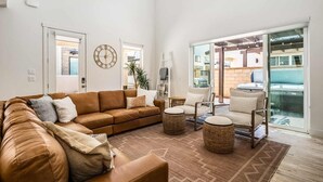 A spacious living room with a brown leather sofa, two armchairs, and a coffee table. There is a large clock on the wall and a sliding glass door leading to an outdoor area. - Desert Brooke Villa 6 Bedroom Townhouse (St. George)