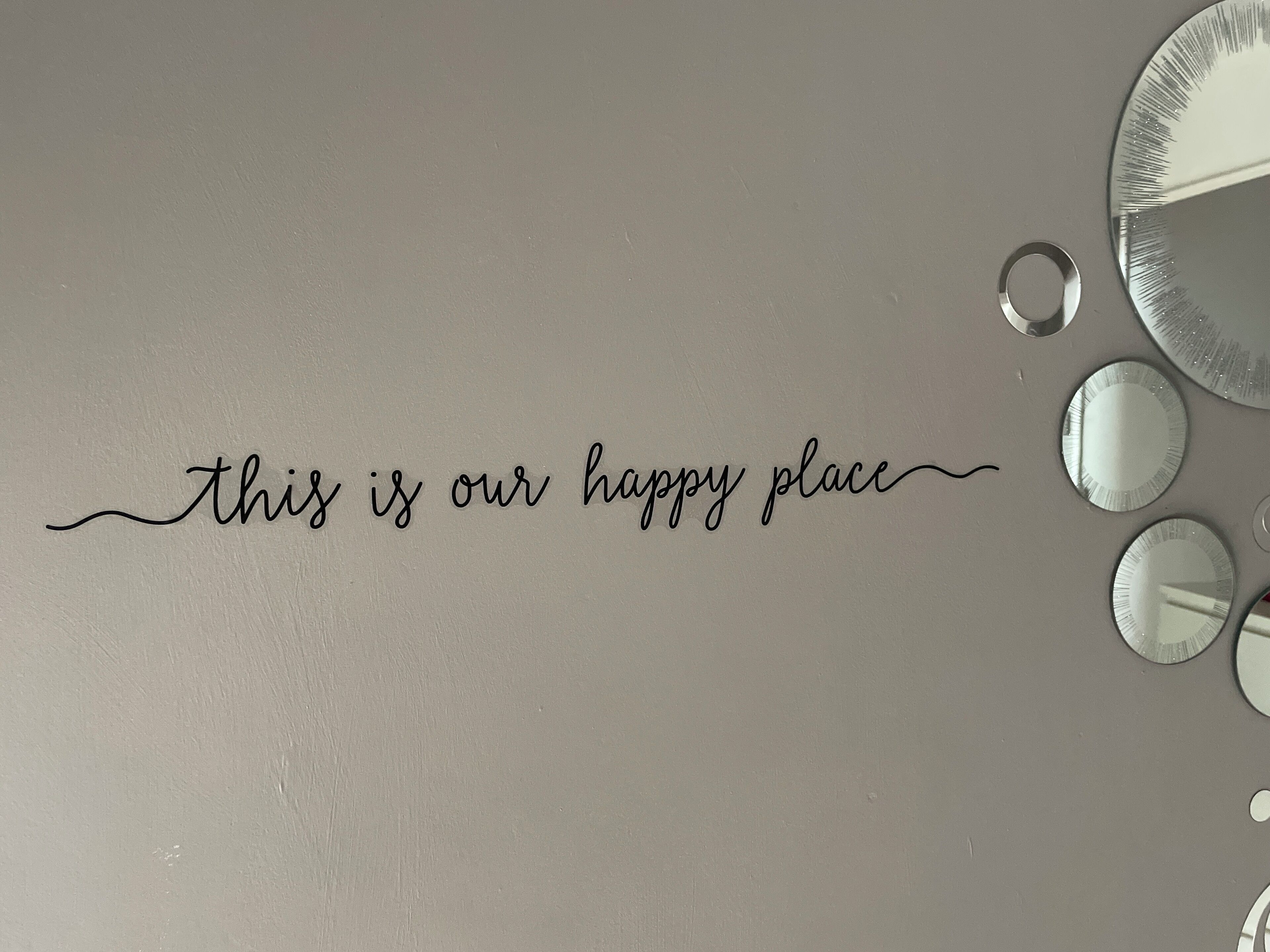 Una pared con el texto "este es nuestro lugar feliz" y varios espejos redondos.
