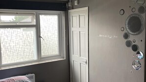 Ein Schlafzimmer mit Bett, Fenster, Tür und einer Wand mit dekorativen Spiegeln.